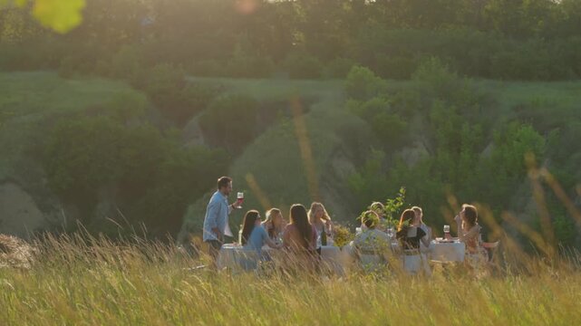 Friends enjoying festive food and conversation in meadow. Concept of communal meals, authentic lifestyle, gastronomy and outdoor hospitality.