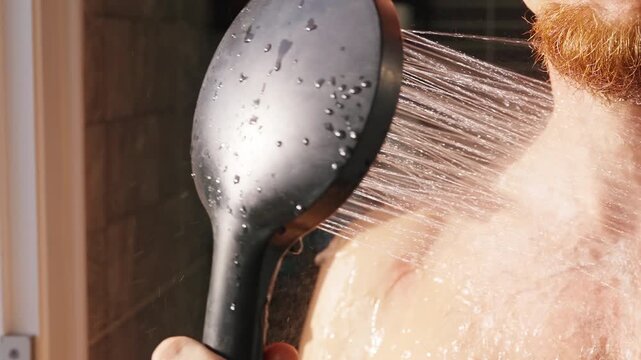 Bearded Man Rinses His Shoulder With a Handheld Shower in a Tiled Bathroom, Showing Personal Hygiene and Wellbeing