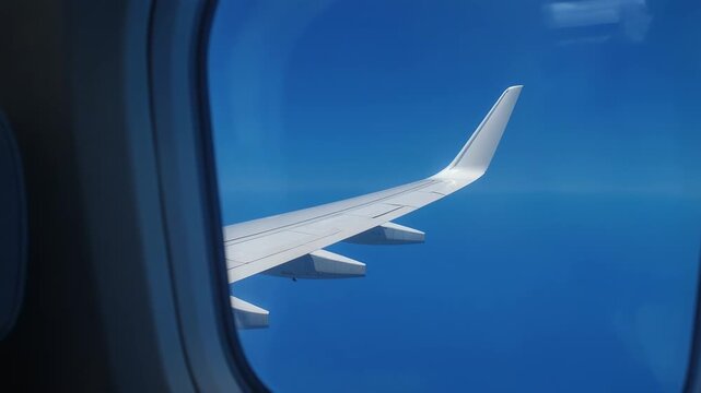Airplane wing glides smoothly through clear blue sky during daytime flight over ocean