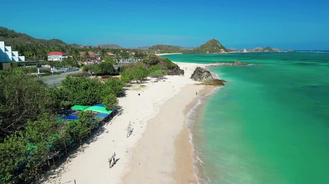 Aerial drone view of Kuta Beach Lombok Indonesia on a sunny day showing white sand surf waves and turquoise ocean waters