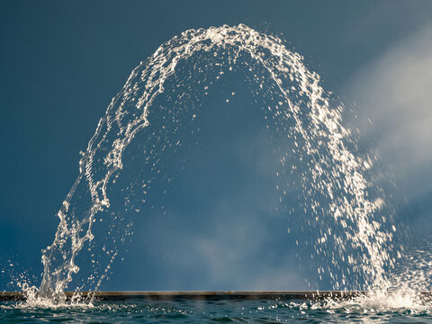 A dynamic water fountain jet creating a perfect arch against a blue sky.