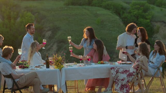 Happy company gathering around table during golden hour. Concept of summer celebration, friendship, outdoor catering and premium lifestyle.