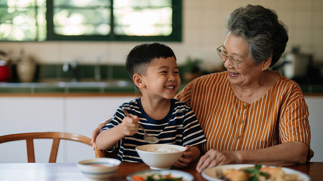 Young Asian boy happily sharing a meal with his grandmother at a family table, intergenerational love, cultural family traditions, healthy eating, grandmother and grandson,