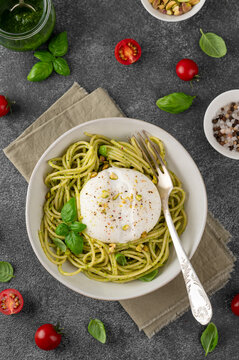 Pesto spaghetti with burrata, basil leaves, pistachios and cherry tomatoes in a bowl. Top view. Italian food. Healthy homemade meal.