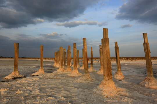 Wooden posts in salt lake surface with dramatic clouds at sunset