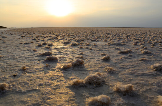 Golden sunset illuminates vast salt flats with textured ground and distant horizon