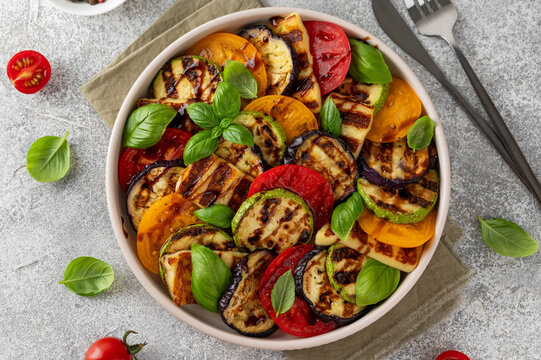 Grilled vegetable salad with zucchini, eggplant, tomatoes, halloumi cheese, basil and balsamic glaze on a plate on a concrete background. Healthy food. Top view.