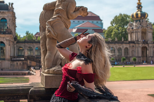 Woman in elegant deep red velvet corset top and black lace cape posing at a historic palace courtyard, fashion and premium lifestyle concept with modern vintage aesthetic