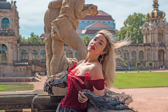 Woman in elegant deep red velvet corset top and black lace cape posing at a historic palace courtyard, fashion and premium lifestyle concept with modern vintage aesthetic