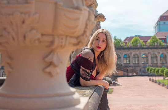Woman in elegant deep red velvet corset top and black lace cape posing at a historic palace courtyard, fashion and premium lifestyle concept with modern vintage aesthetic