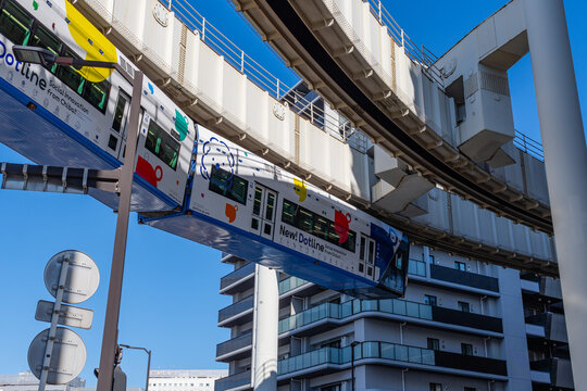 Chiba, Japan-February 1, 2026: Modern suspended monorail train traveling above a bustling city street on a bright sunny day with car and street traffic below.