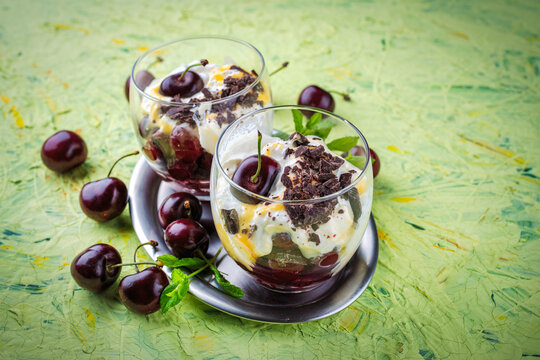 Parfait dessert with whipped cream,  mascarpone fresh cream cheese, dark chocolate and sour and sweet cherries served as close-up in a glass