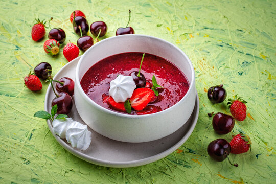 Strawberry and cherry fruit soup with meringues and peppermint served as close-up in a design bowl
