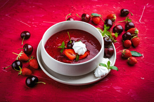 Strawberry and cherry fruit soup with meringues and peppermint served as close-up in a design bowl