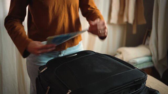 Anonymous young woman in a hotel reviewing a map to decide where to travel, then folding it and placing it inside her suitcase as part of her trip preparation.