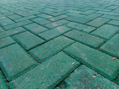 Close-up angled view of green interlocking concrete paving blocks arranged in a herringbone pattern. Textured pavers used for sidewalks, parks, and outdoor landscaping.