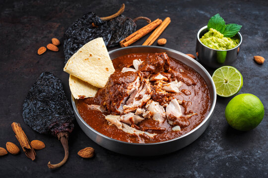 Traditional authentic artisan spicy chicken mole poblano in a bowl with avocado guacamole and fresh tortilla served as close-up on a design plate