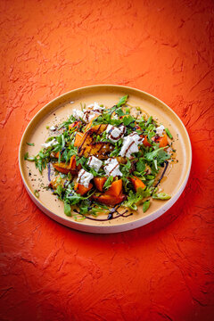 Fresh made spring mixed salad with arugula, sweet potato, feta sheep milk cheese and caramelized nectarines with balsamico cream served as close-up on a design plate