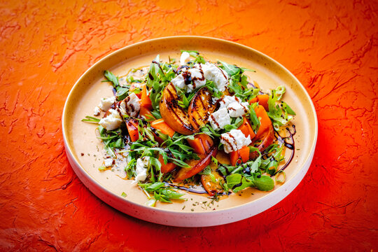 Fresh made spring mixed salad with arugula, sweet potato, feta sheep milk cheese and caramelized nectarines with balsamico cream served as close-up on a design plate