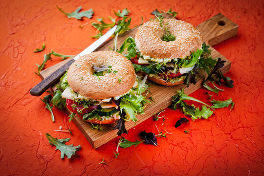 Classic fingerfood fastfood snack -  traditional sesam bagels - bread rolls sandwich with avocado guacamole, cheese and vegetable salad served on wooden board