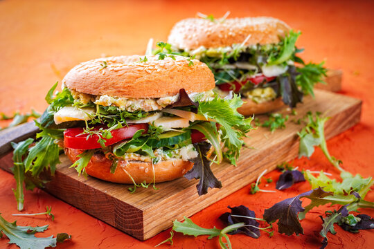 Classic fingerfood fastfood snack -  traditional sesam bagels - bread rolls sandwich with avocado guacamole, cheese and vegetable salad served as close-up on a wooden board
