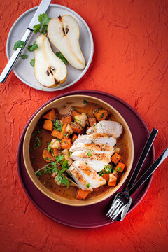 Braised chicken breast fillet with roasted vegetables pumpkin, pear and sweet potato in wine sauce served as top view in a design bowl