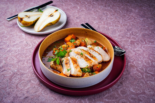 Braised chicken breast fillet with roasted vegetables pumpkin, pear and sweet potato in wine sauce served as close-up in a design bowl