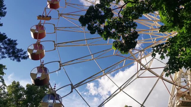 Ferris wheel against blue sky with green trees in amusement park