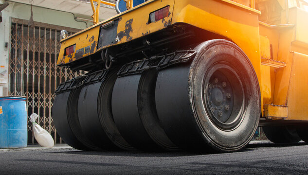 Yellow road roller compactor working on freshly paved asphalt, showing heavy construction machinery used for roadwork, pavement repair, street maintenance and infrastructure development.