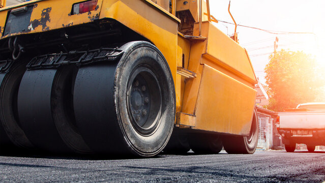 Yellow road roller compactor working on freshly paved asphalt, showing heavy construction machinery used for roadwork, pavement repair, street maintenance and infrastructure development.
