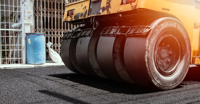 Yellow road roller compactor working on freshly paved asphalt, showing heavy construction machinery used for roadwork, pavement repair, street maintenance and infrastructure development.