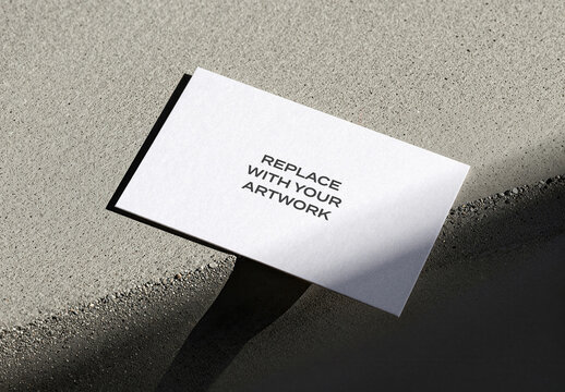 Business card mockup on a textured concrete surface with strong directional lighting and defined shadows, realistic stationery presentation, template for graphic design, print media