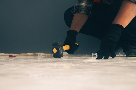 The craftsman is using a hammer to break tiles and level the surface.