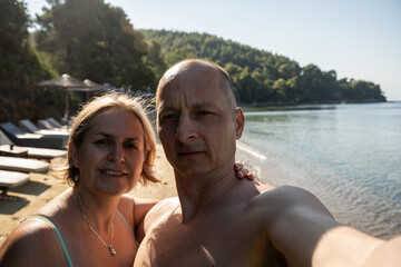 Fototapeta premium Portrait of a happy mature couple taking a selfie and having fun at the beach