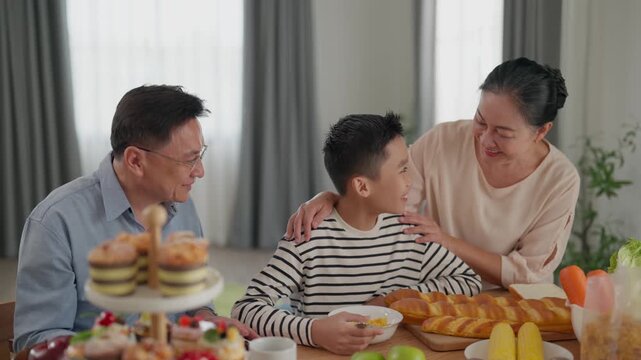 Family asian indoor dining table together smiling child parent grandparent at home breakfast with bread pastry cereal bowl tea coffee fruit in cozy casual living room near curtain window