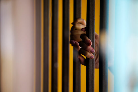 Person's hand gripping prison cell bars with a small cozy blanket on the other side