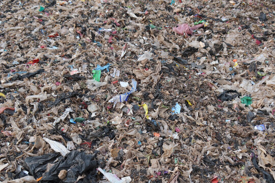 A waste processing facility with a large pile of shredded plastic and mixed municipal waste, representing material prepared for sorting, recycling, or refuse-derived fuel production.