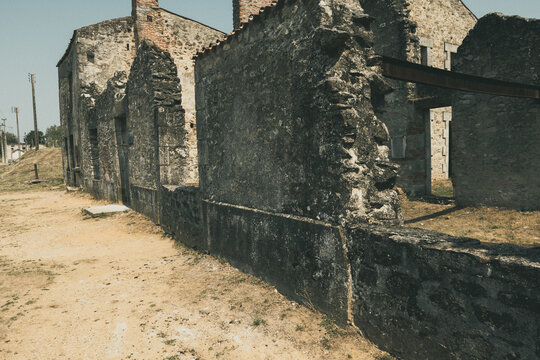 Broken Street-Row of roofless stone ruins lining a quiet street in the preserved martyr village of Oradour-sur-Glane, sunlit walls and empty doorways, Oradour-sur-Glane, Haute-Vienne, France.