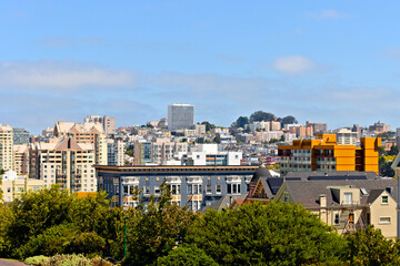 Obraz premium Dense San Francisco neighborhoods and varied architecture rise beyond leafy trees under a bright blue sky with low summer clouds.