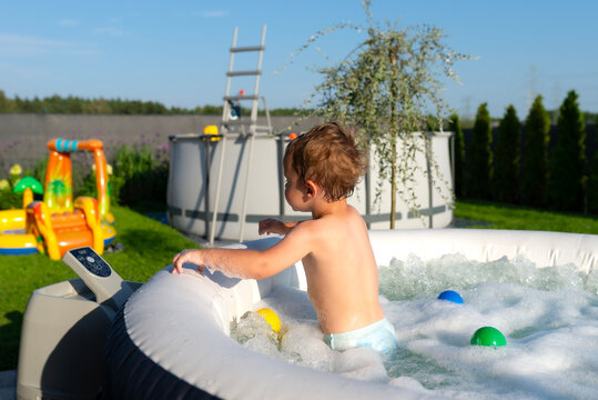 Toddler boy playing in outdoor inflatable jacuzzi with bubbles