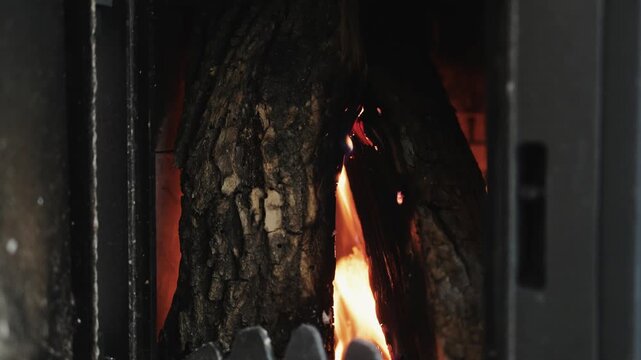 Warm fire burning in a rustic fireplace, with a large natural log glowing among bright flames. Close-up view of a traditional wood-burning stove creating a warm indoor atmosphere.