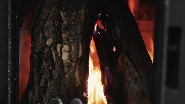 Close-up of flames burning around a large piece of firewood inside a rustic stove. Bright fire and glowing embers create a warm winter scene in a traditional home.