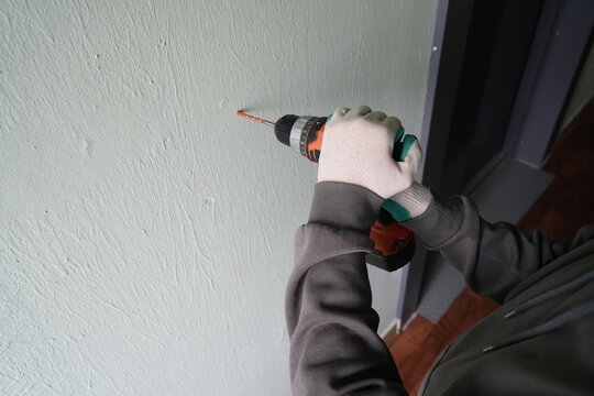 Top view of hands drilling stucco wall with cordless drill