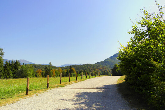 Scenic view of a lush green meadow and gravel path bordered by wooden posts in Val di Sella near Arte Sella (SELLA ART), Trentino, Northern Italy, with mountains in the background under a sunny 