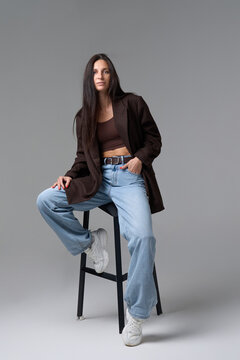 Trendy mid adult woman in oversized brown blazer sitting on black high stool