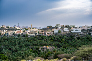 Naklejka premium Traditional mountain village surrounded by lush date palm plantations in Oman, rural travel, local culture, oasis landscape and heritage tourism concept