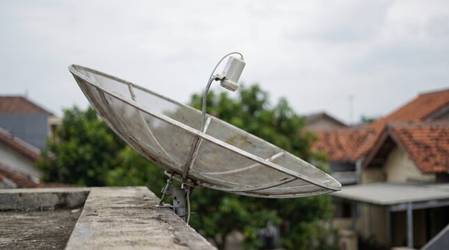 Satellite dish on residential rooftop, metal parabolic antenna for television signal, telecommunications equipment in urban neighborhood