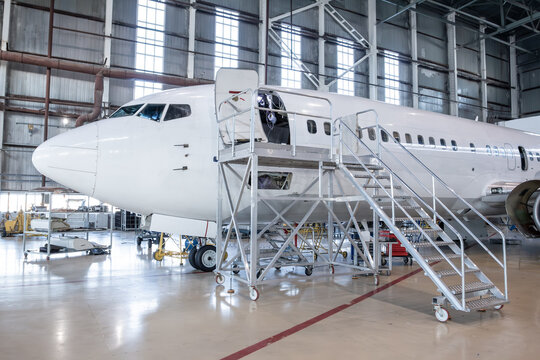 White passenger aircraft in the aviation hangar. Jet plane under maintenance. Checking mechanical systems for flight operations