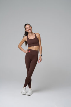Full length portrait of smiling fit woman in brown sportswear standing in studio