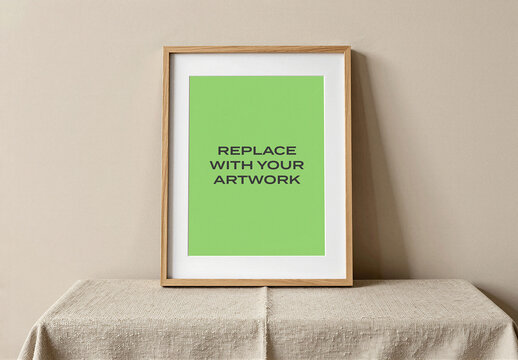 Vertical framed poster mockup with placeholder text displayed on a fabric-covered table against neutral wall interior, realistic art presentation for graphic design and branding, template